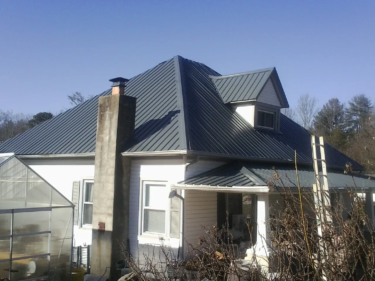 Dark blue standing seam metal roof on a white farmhouse with dormer — Slate & Tile Roof Repair by Roofing Brothers in Marne
